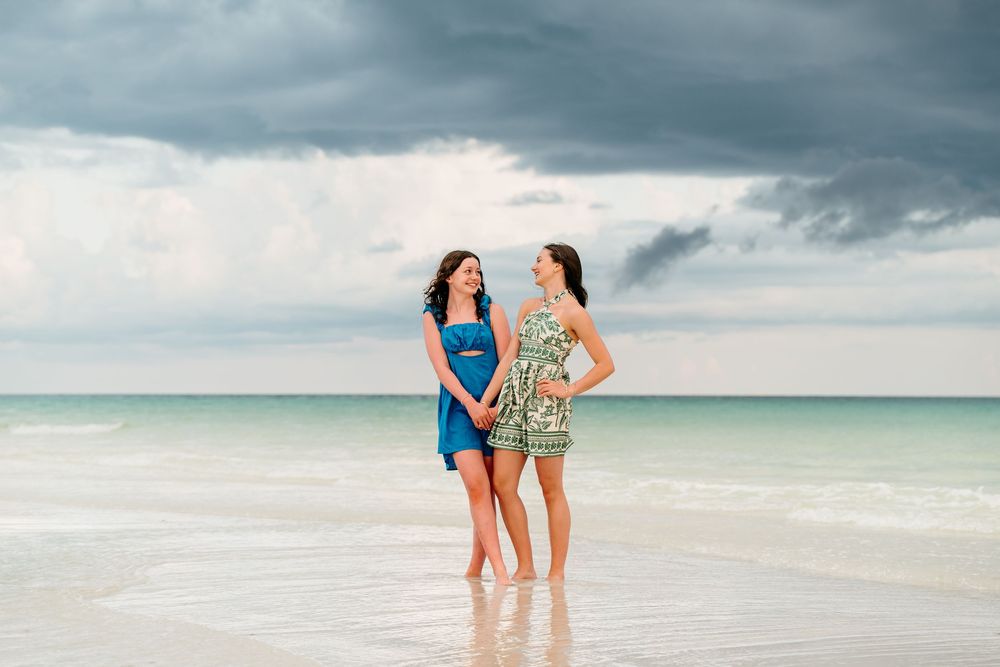Family members walk together along a pristine white sand beach under dramatic storm clouds at sunset.