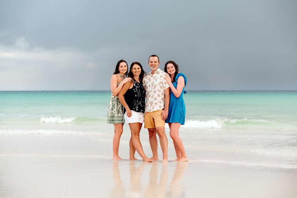 Group enjoying a sunny day on a white sandy beach with turquoise ocean waters in the background.