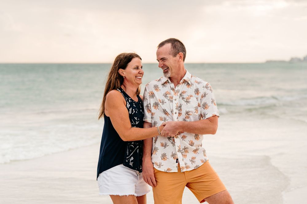 Happy couple laughing and embracing while enjoying a romantic evening on a sandy beach at sunset.