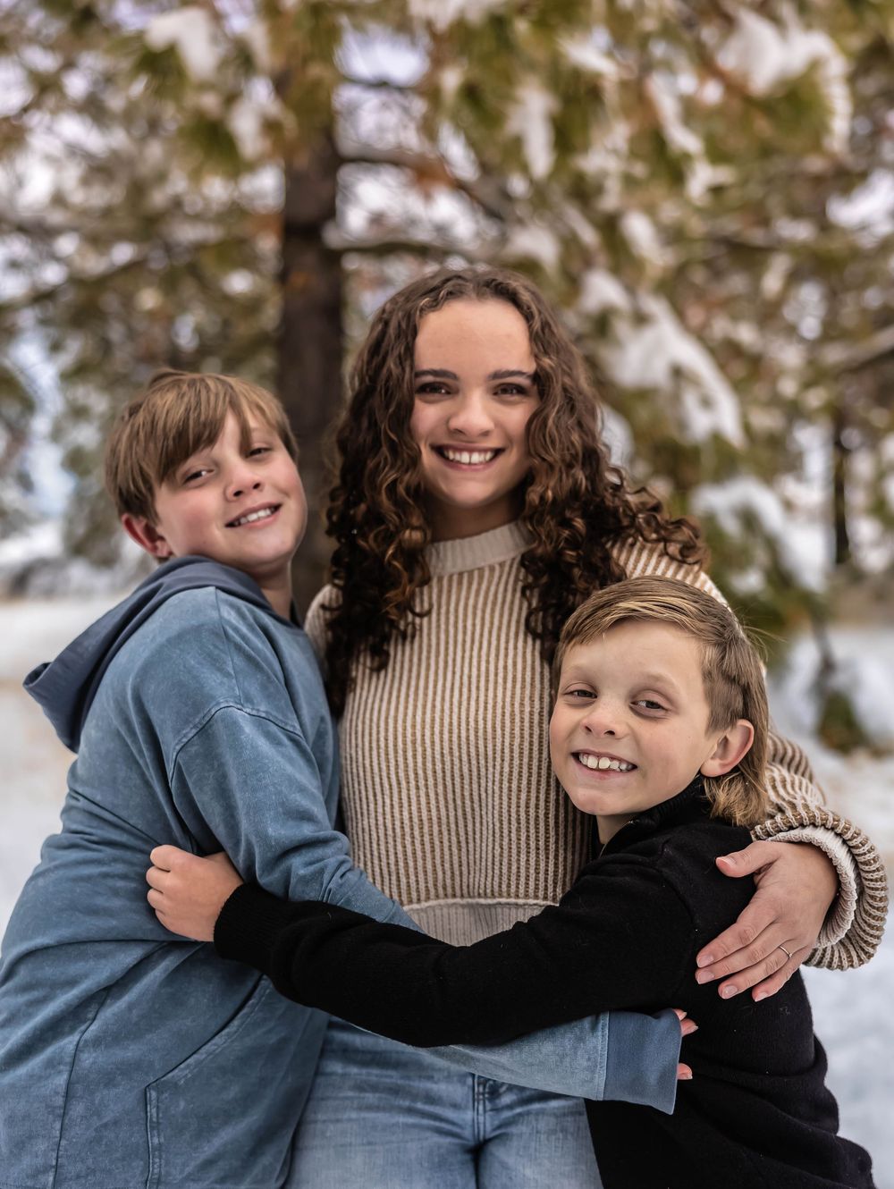 Candid winter family photo showing warm embraces in front of snow-covered trees.