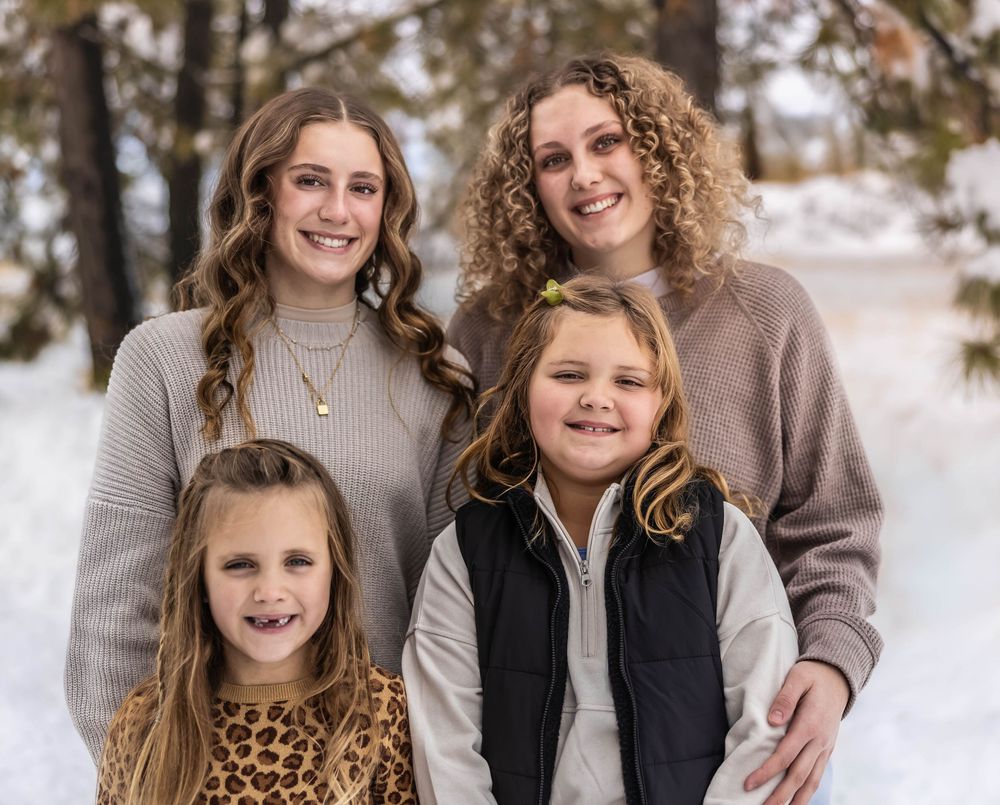 Family portrait in coordinated winter outfits against snow-covered forest background.