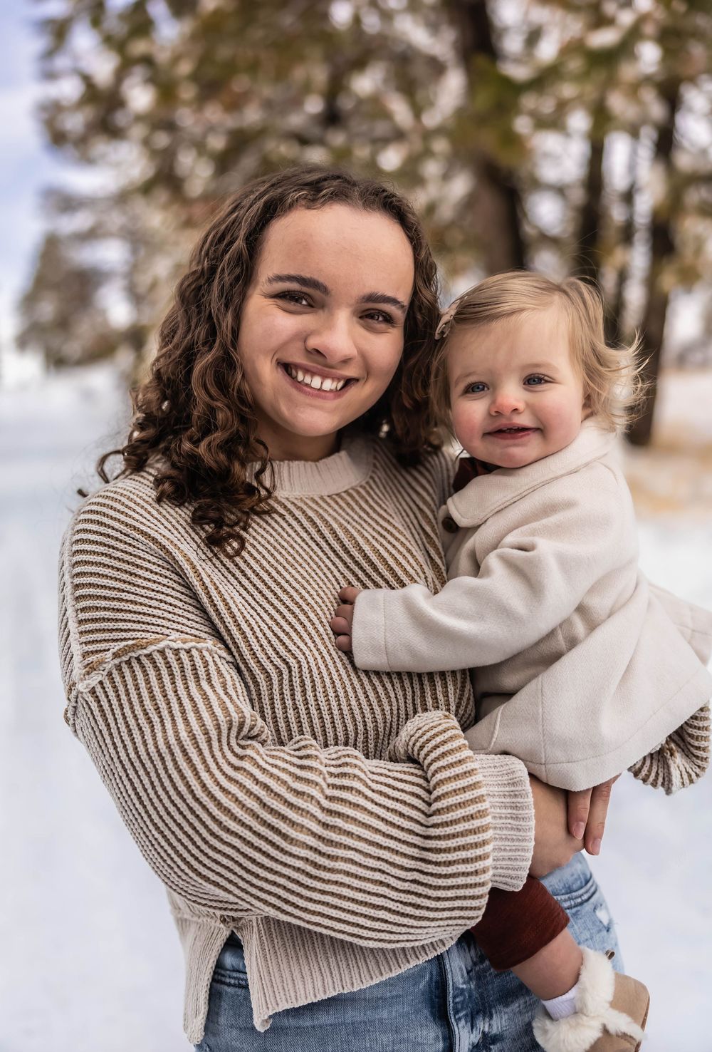 Two people in winter sweaters share playful embraces against a snowy forest backdrop.
