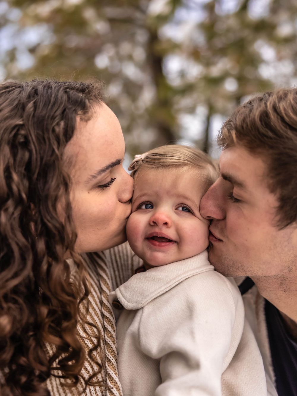 Sweet family moment captured with kisses in a snowy forest setting.