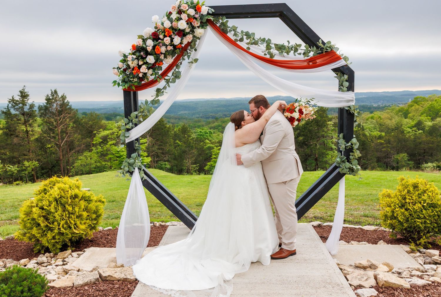 A romantic outdoor wedding ceremony at a mountain overlook with floral arch and white draping against scenic views at the Atrium in Branson.