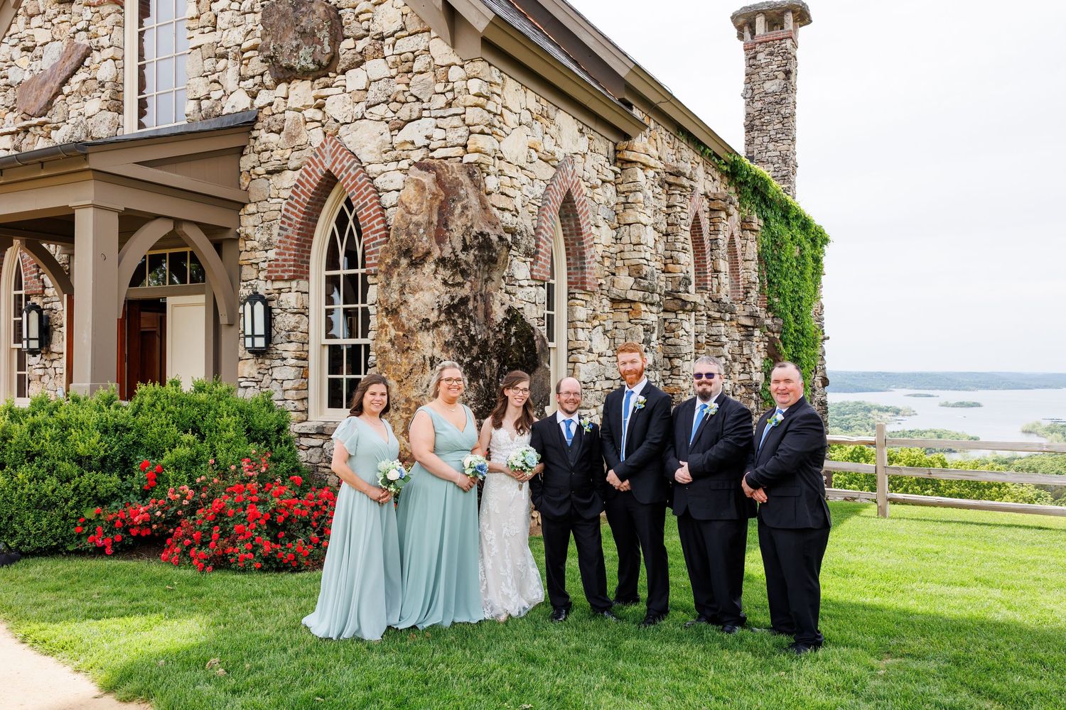 Wedding party poses on a scenic coastal property with rustic stone buildings and blooming gardens in the background at Top of the Rock.