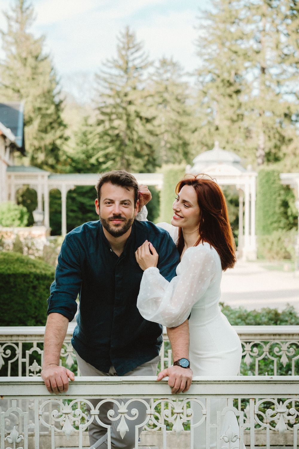 Couple sharing intimate moment while leaning on ornate white railing outdoors.