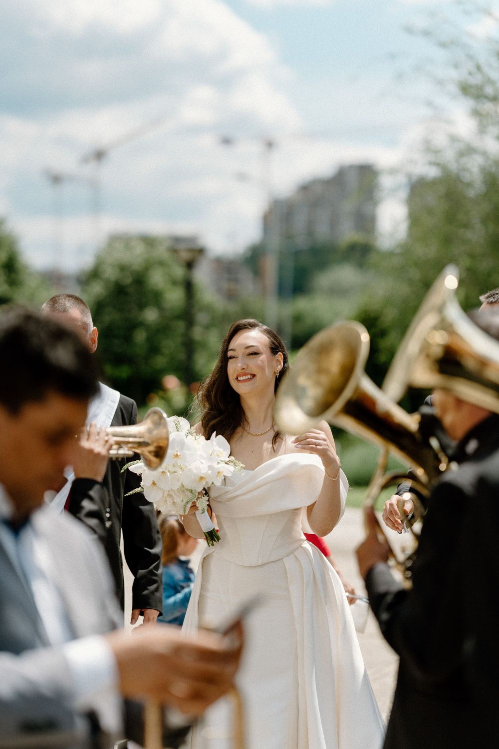 Joyous wedding celebration outdoors with musicians playing brass instruments while couple shares happy moment in bright sunlight.