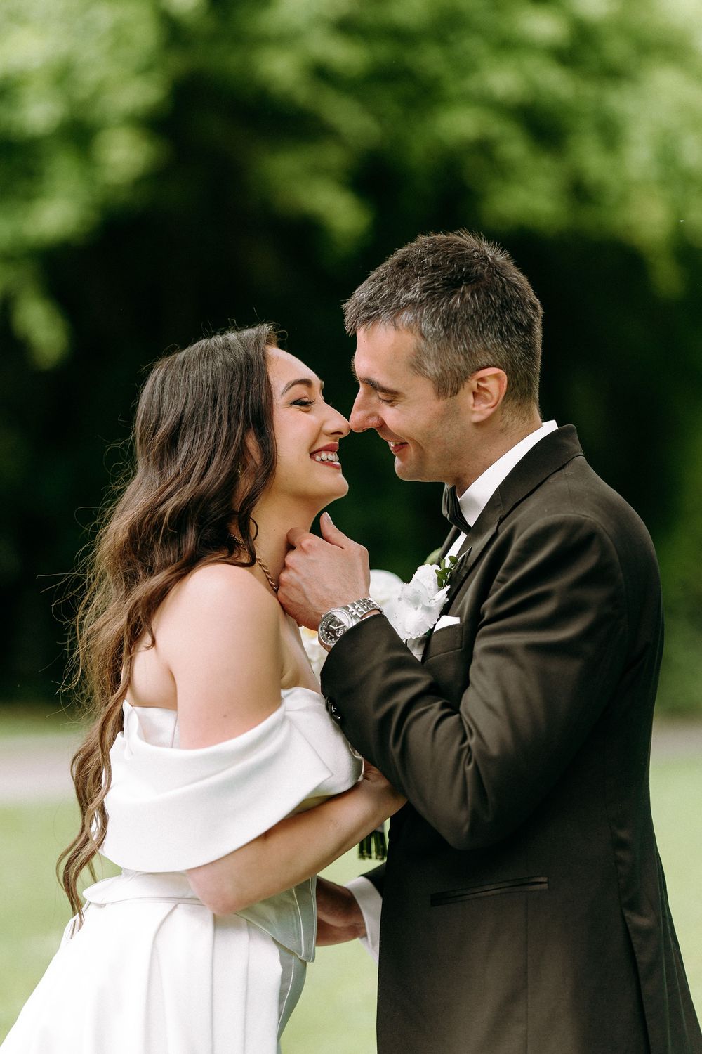 A romantic wedding moment captured outdoors with the couple sharing a joyful laugh in formal attire.