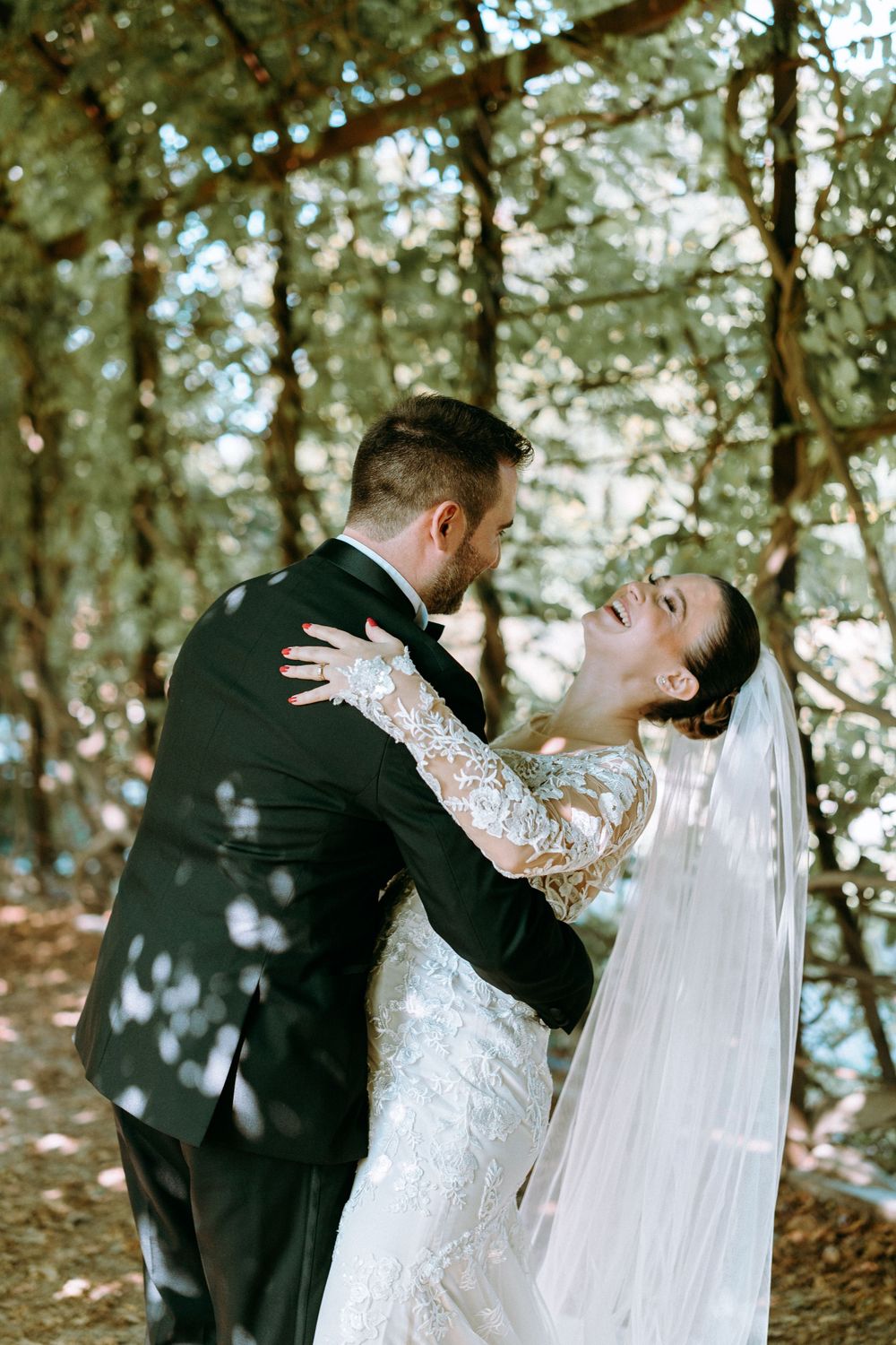 Romantic woodland wedding portrait with sunlight filtering through trees.