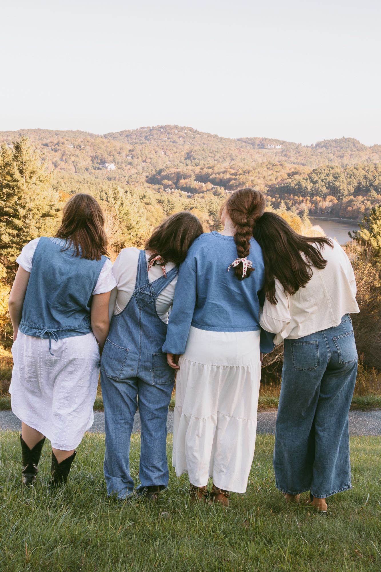 Group wearing blue jeans and white shirts standing with arms around each other overlooking mountains. Luxury wedding photographer NC