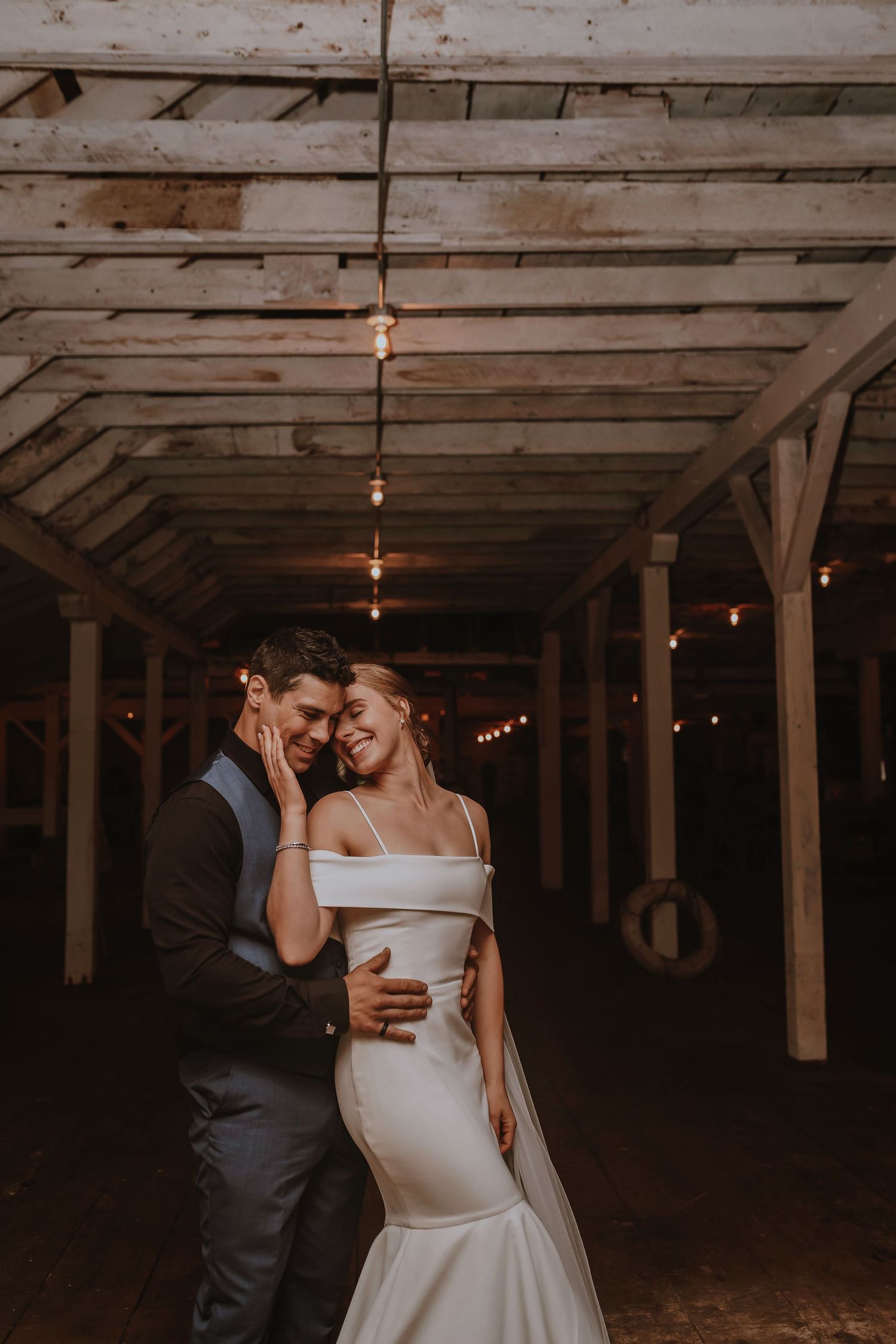Romantic wedding photo in rustic venue with string lights and wooden beams.