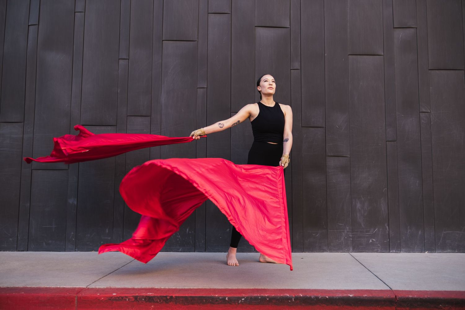 Senior with color guard flags and black top performs dramatic movement against dark wall while red flag fabric billows through air.