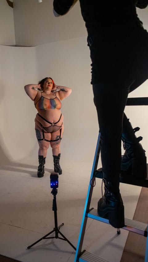 Studio photoshoot setup with lighting equipment and model against white backdrop.