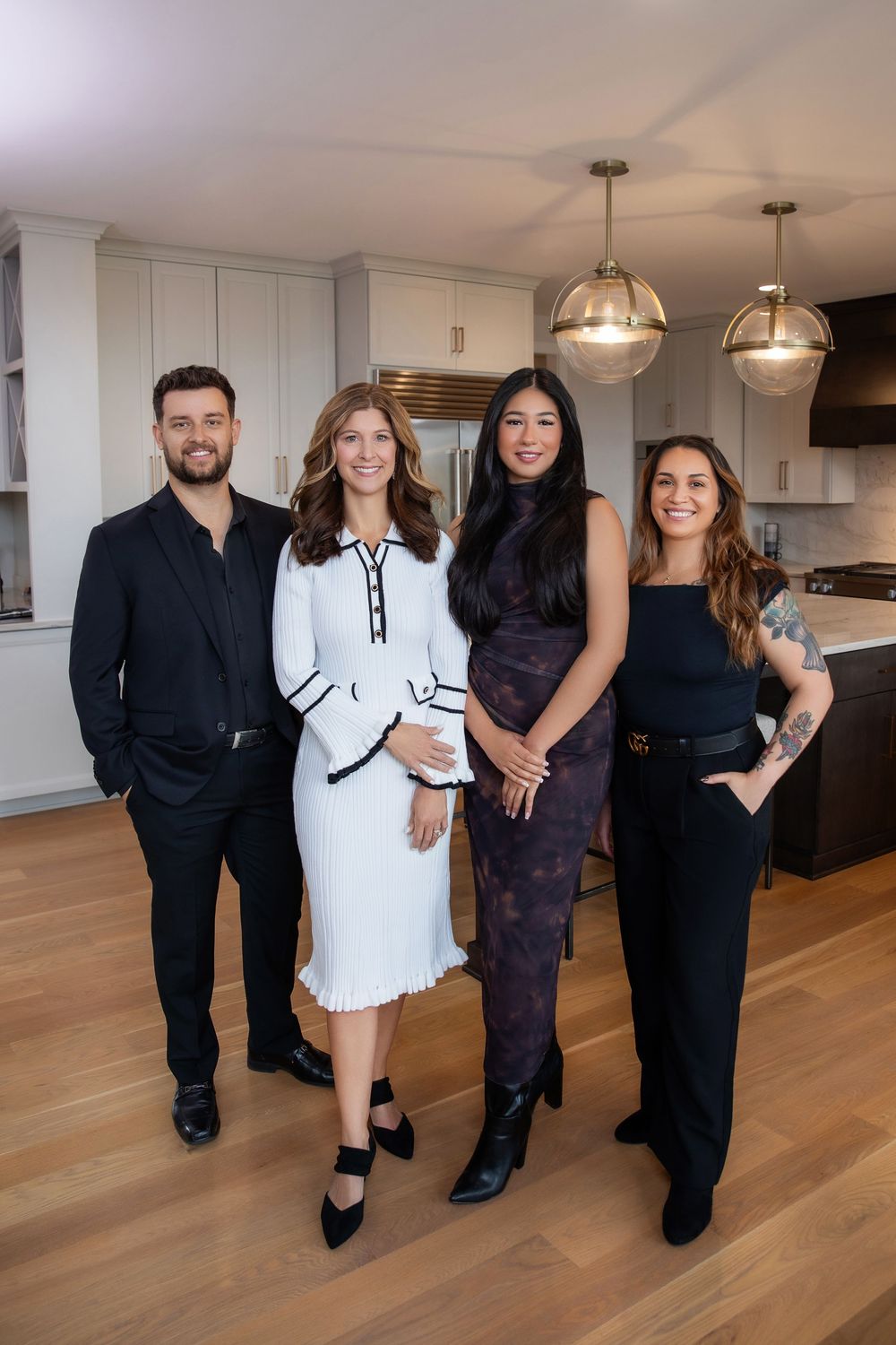 A group of professionals pose together in a modern kitchen with hardwood floors and pendant lighting.