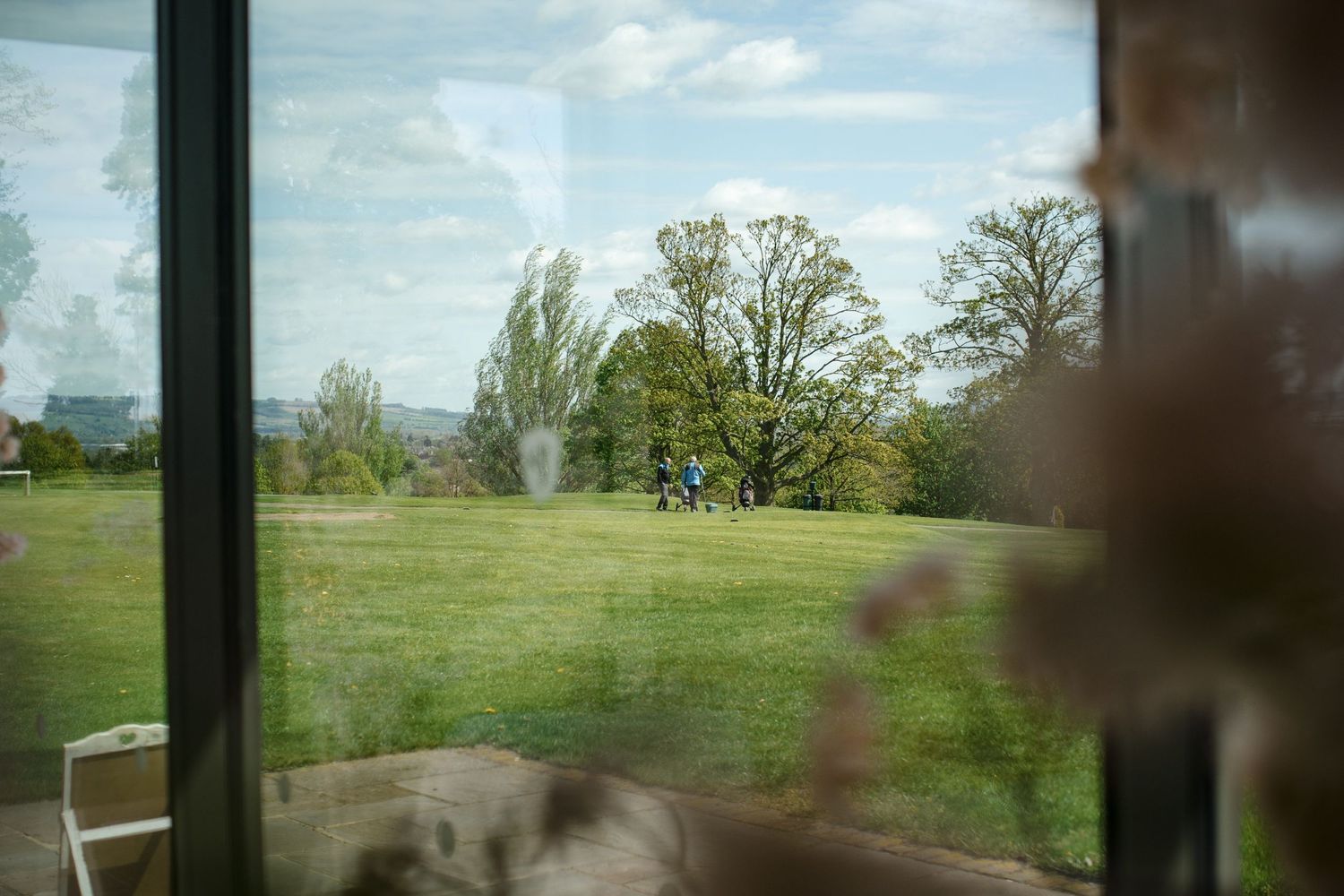 View through window of green Fox Harb'r Resort landscape with tall trees and grassy field on a sunny day during a wedding.