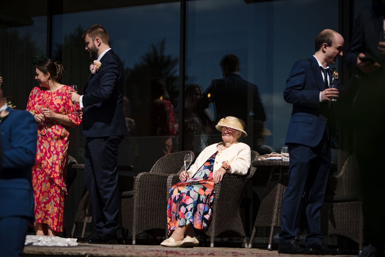 People gathered on an outdoor patio at Fox Harb'r Resort in formal attire, with someone wearing a sun hat seated in between them at wedding