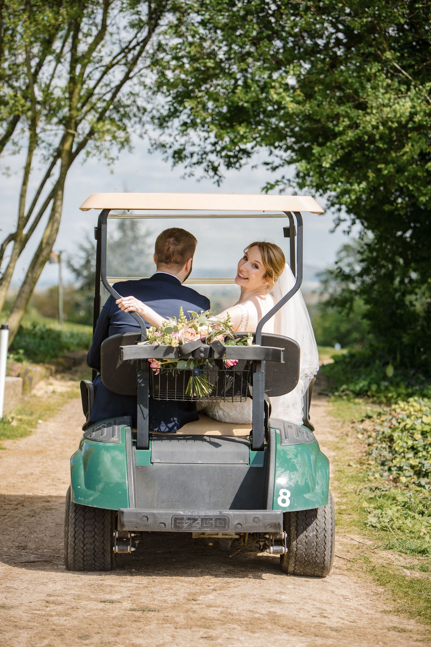 A couple riding in a turquoise golf cart at Fox Harb'r Resort along a rural path with a bouquet of flowers visible in the back.