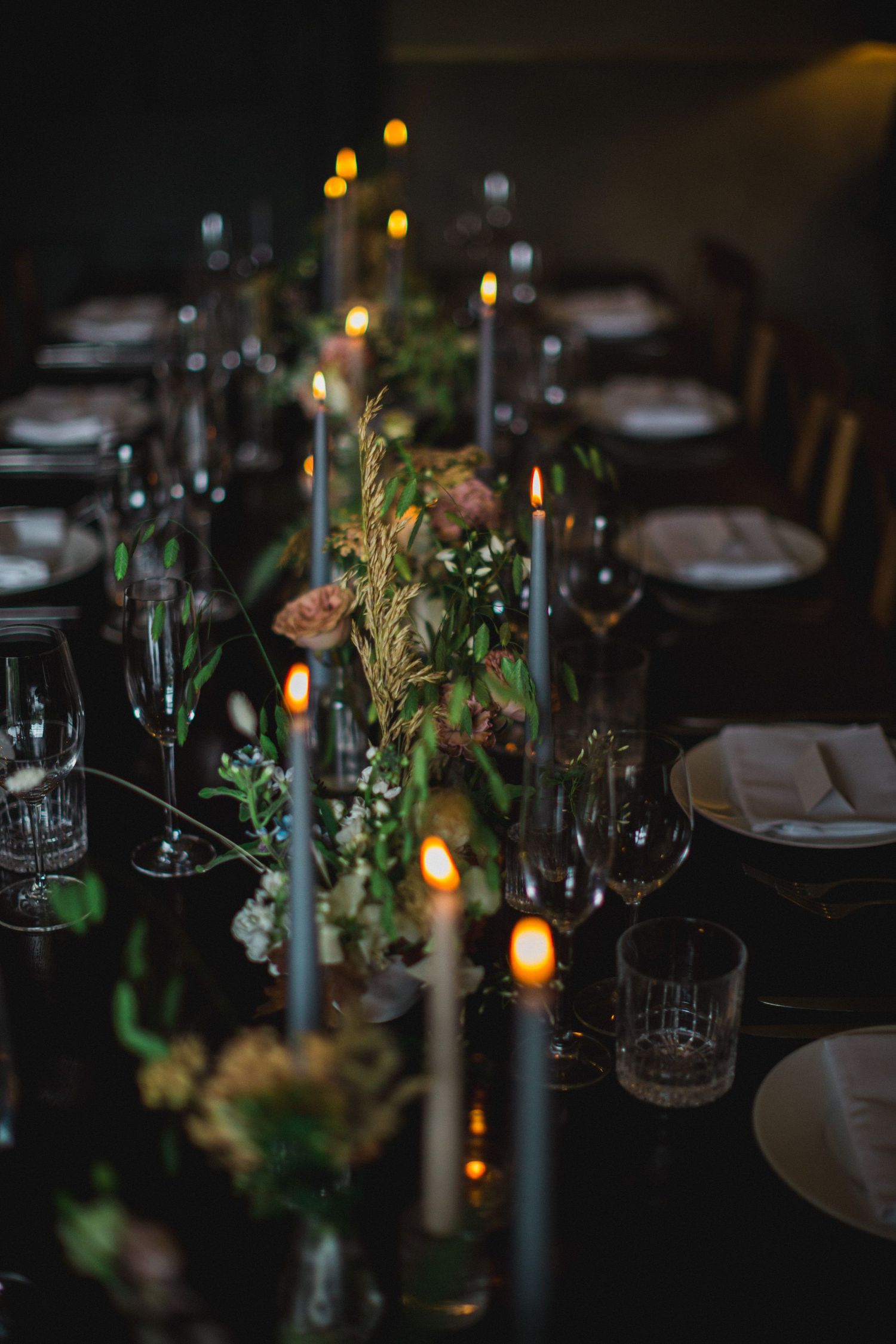 Elegant dinner table setting with candlelight and greenery centerpiece on dark tablecloth with wine glasses and place settings at Fox Harb'r