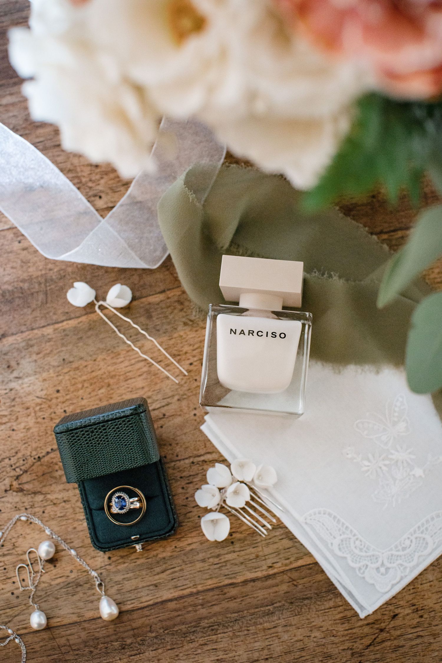 Wedding details with perfume bottle, engagement rings in green box, white ribbon and floral decor on wooden table Nova Scotia wedding venue