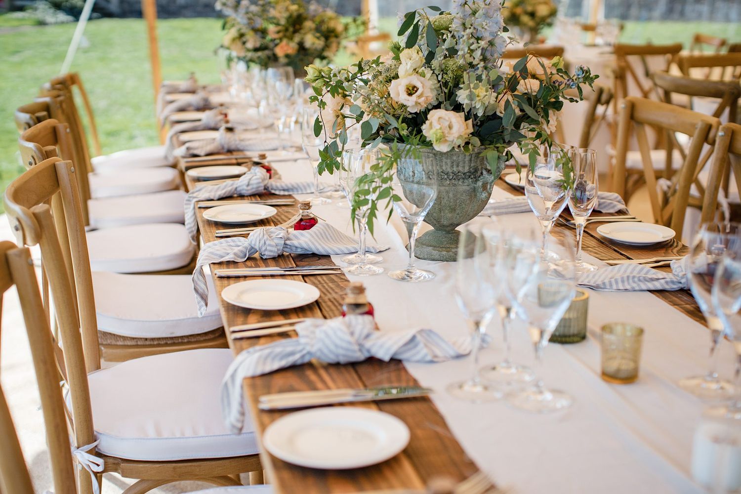 Elegant outdoor wedding table setting with wooden chairs, fresh floral centerpieces, and place settings on white linens at Fox Harb'r Resort
