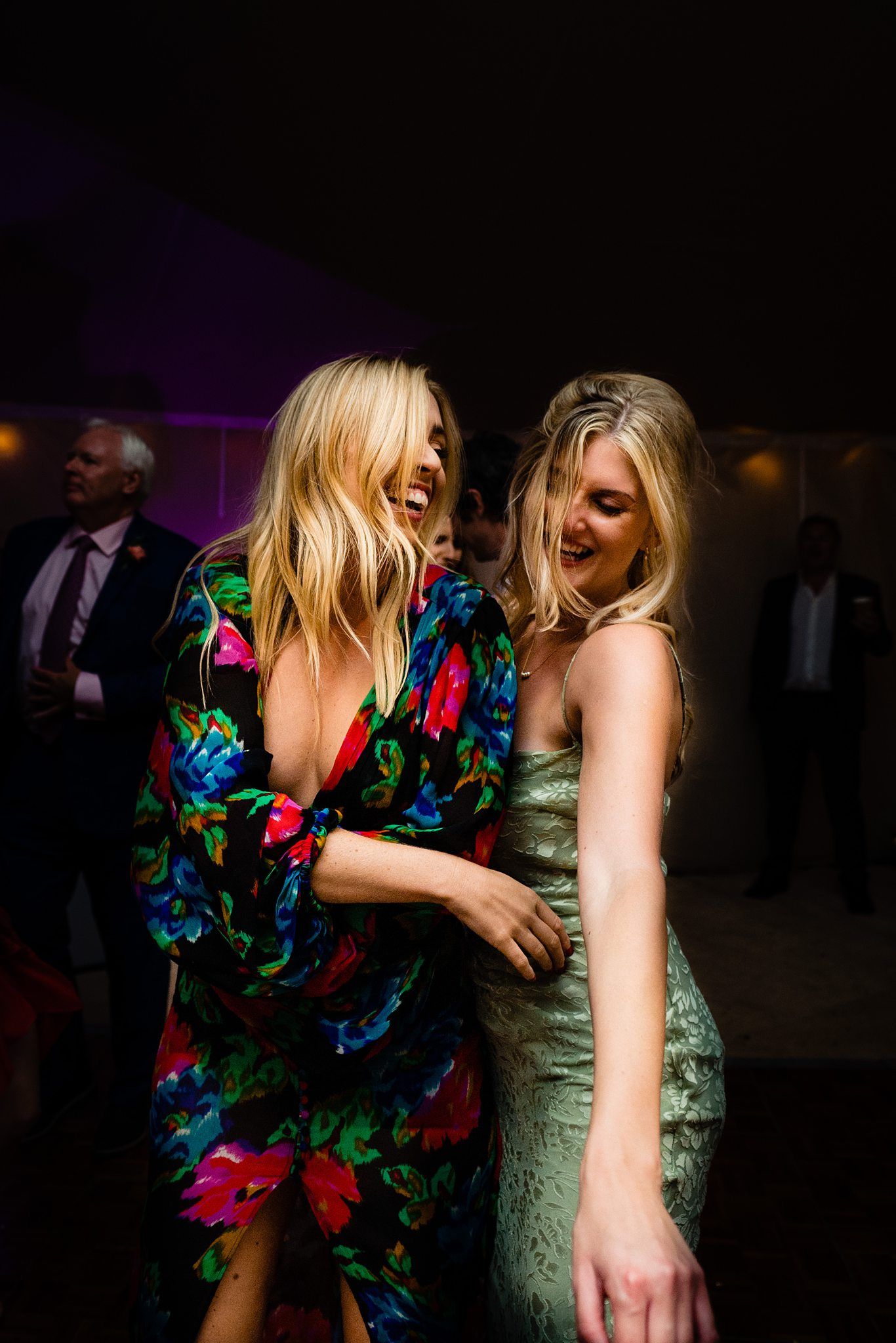 Two women dancing and laughing at a wedding party, one wearing a coloyrful floral dress and one in a light green dress at Fox Harb'r resort