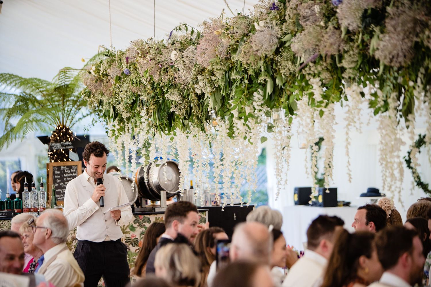 Fox Harb'r Resort Wedding reception under hanging white wisteria flowers with guests seated at tables in elegant marquee setting.