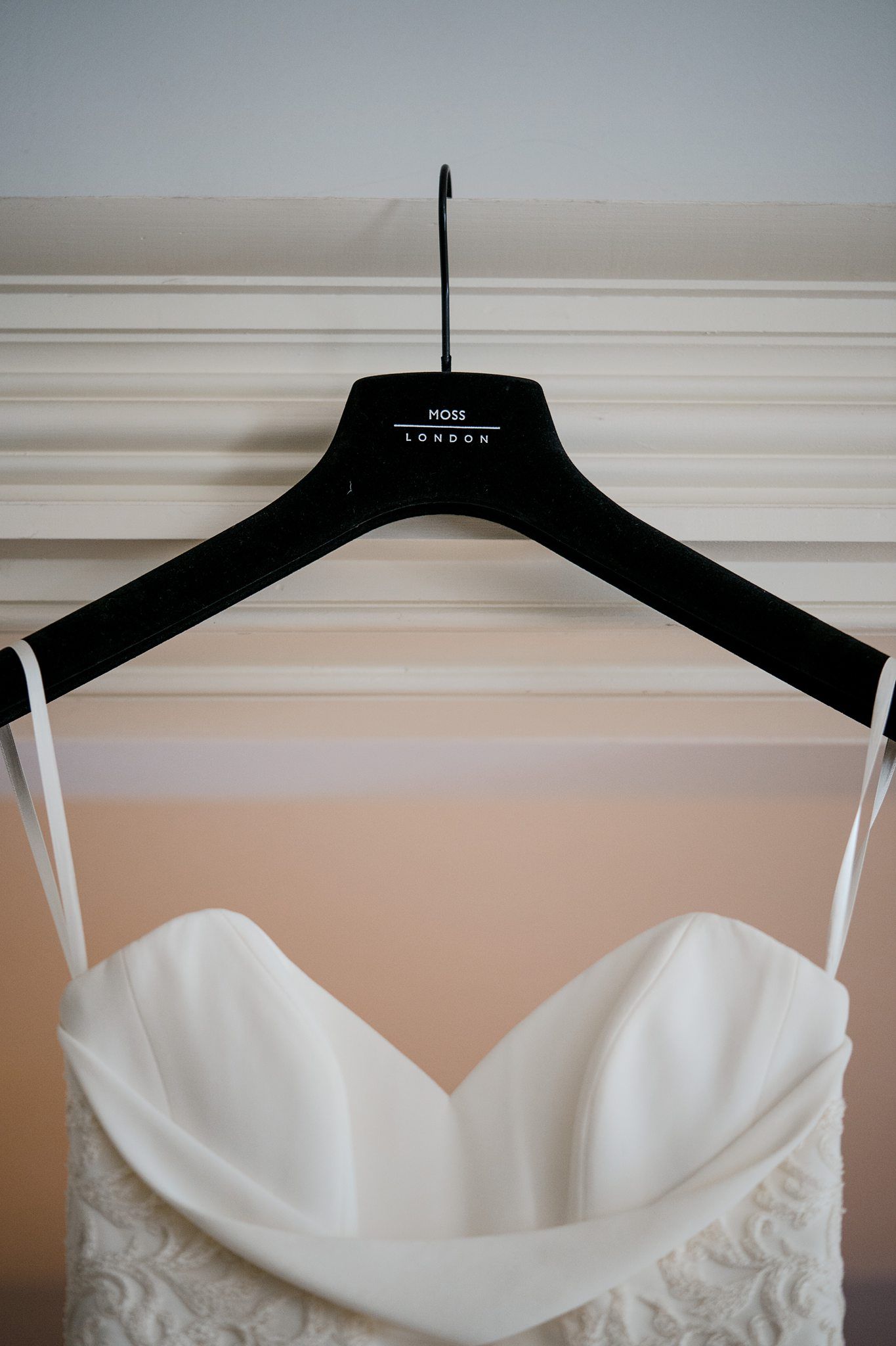 A white wedding dress with sweetheart neckline bodice hangs on a black hanger against a beige wall at Fox Harb'r Resort bridal suit