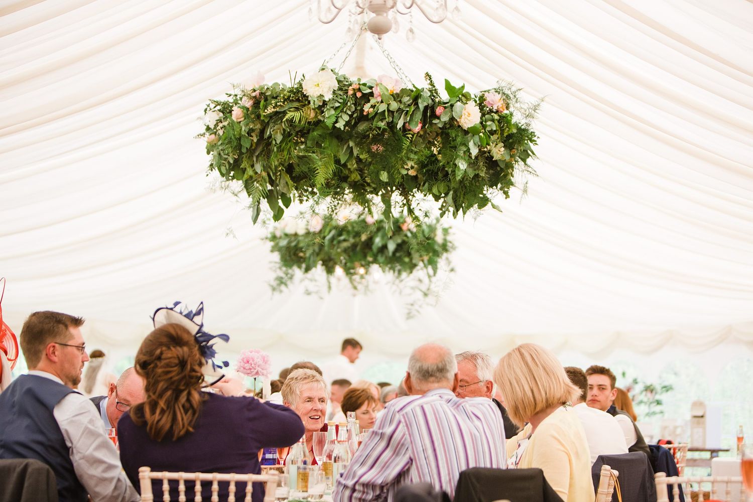 Wedding reception in a white tent with hanging greenery chandelier and guests seated at long tables at Fox Harb'r Resort wedding venue