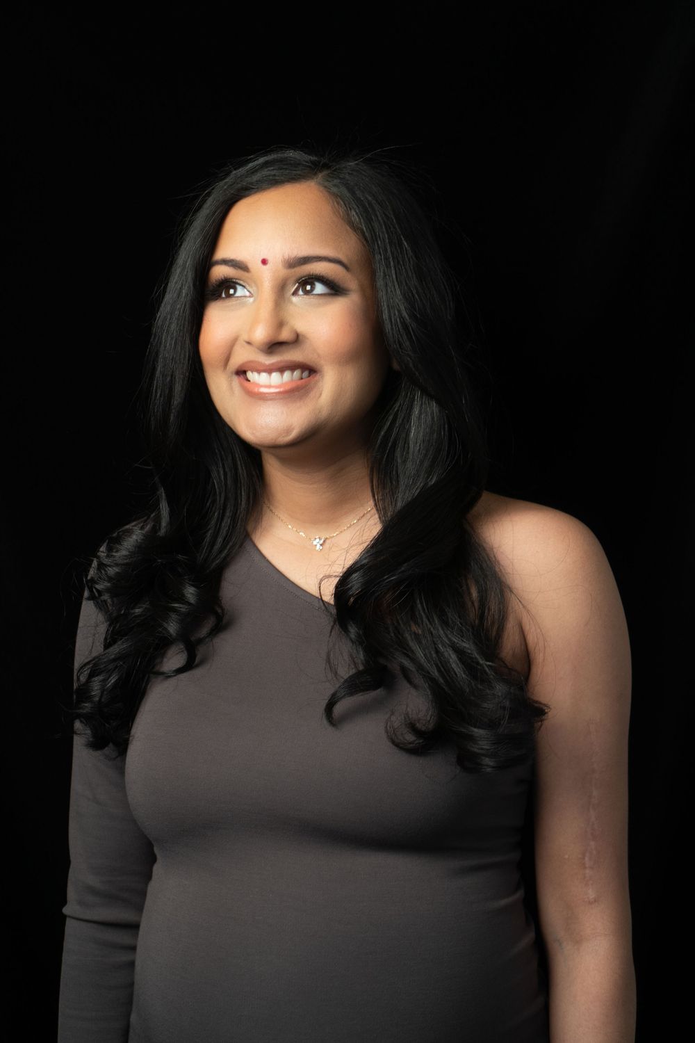 Pregnant woman in brown dress smiling against dark background in studio portrait, looking out away from the camera.