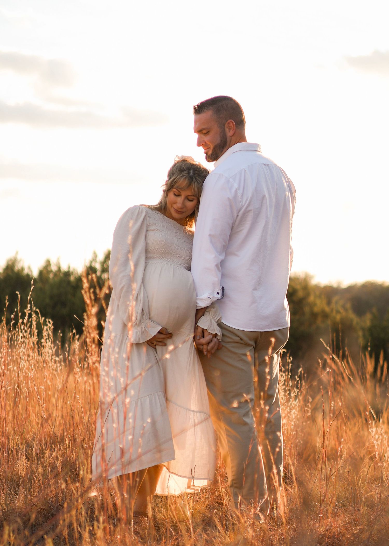 Expecting couple stands together in golden field during sunset maternity photoshoot.
