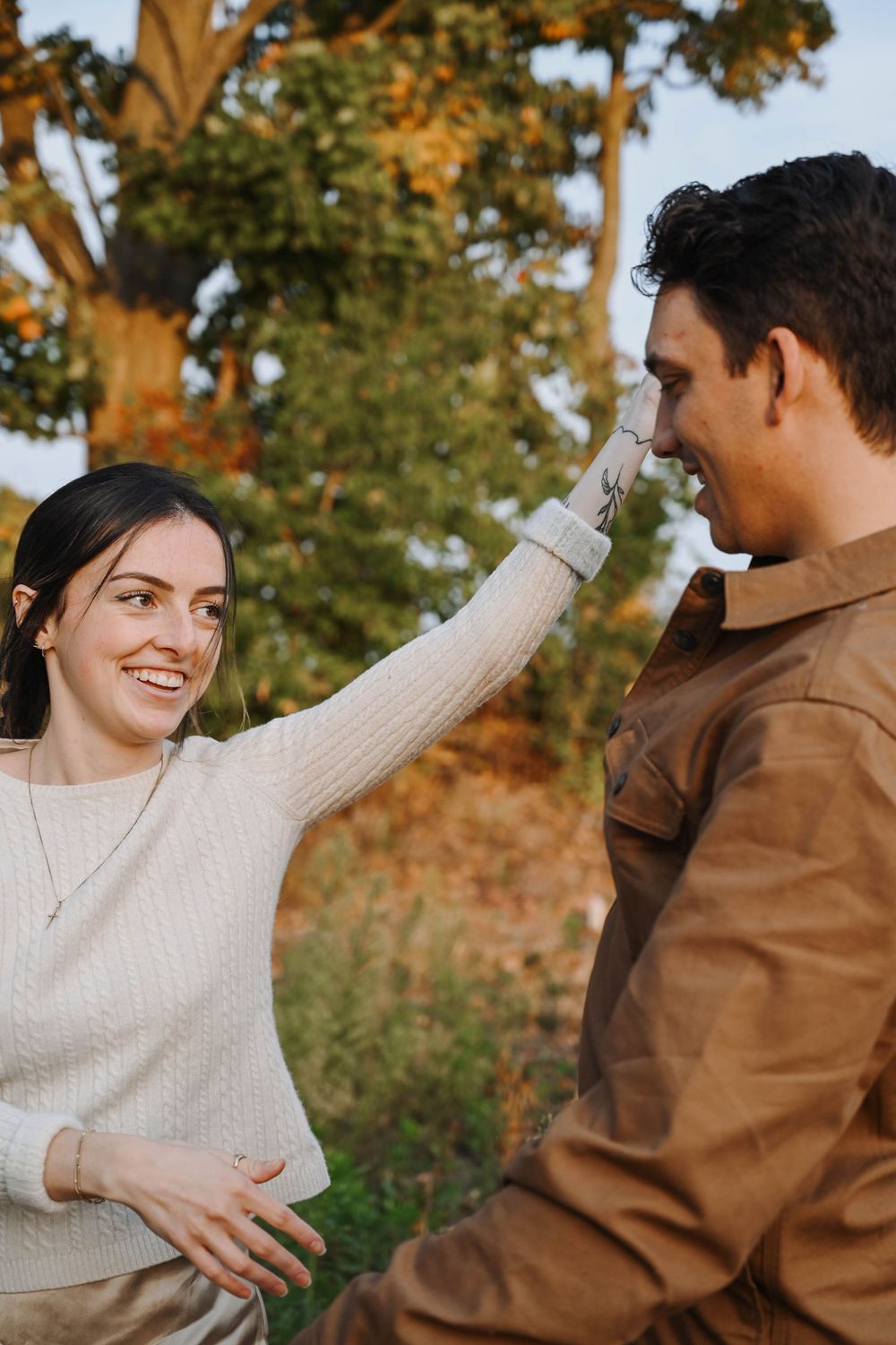 A playful couple shares a joyful moment together outdoors during golden hour in autumn scenery.