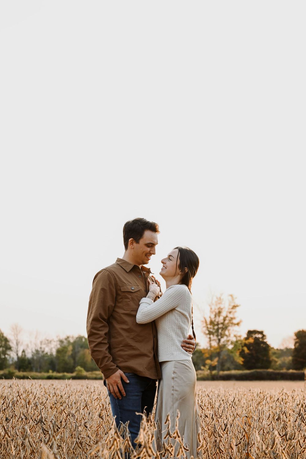 A romantic couple embraces while standing in a golden wheat field at dusk.