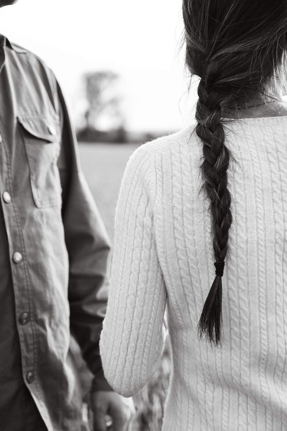 Black and white close-up of two people holding hands, showing a cable knit sweater and braided hair from behind.