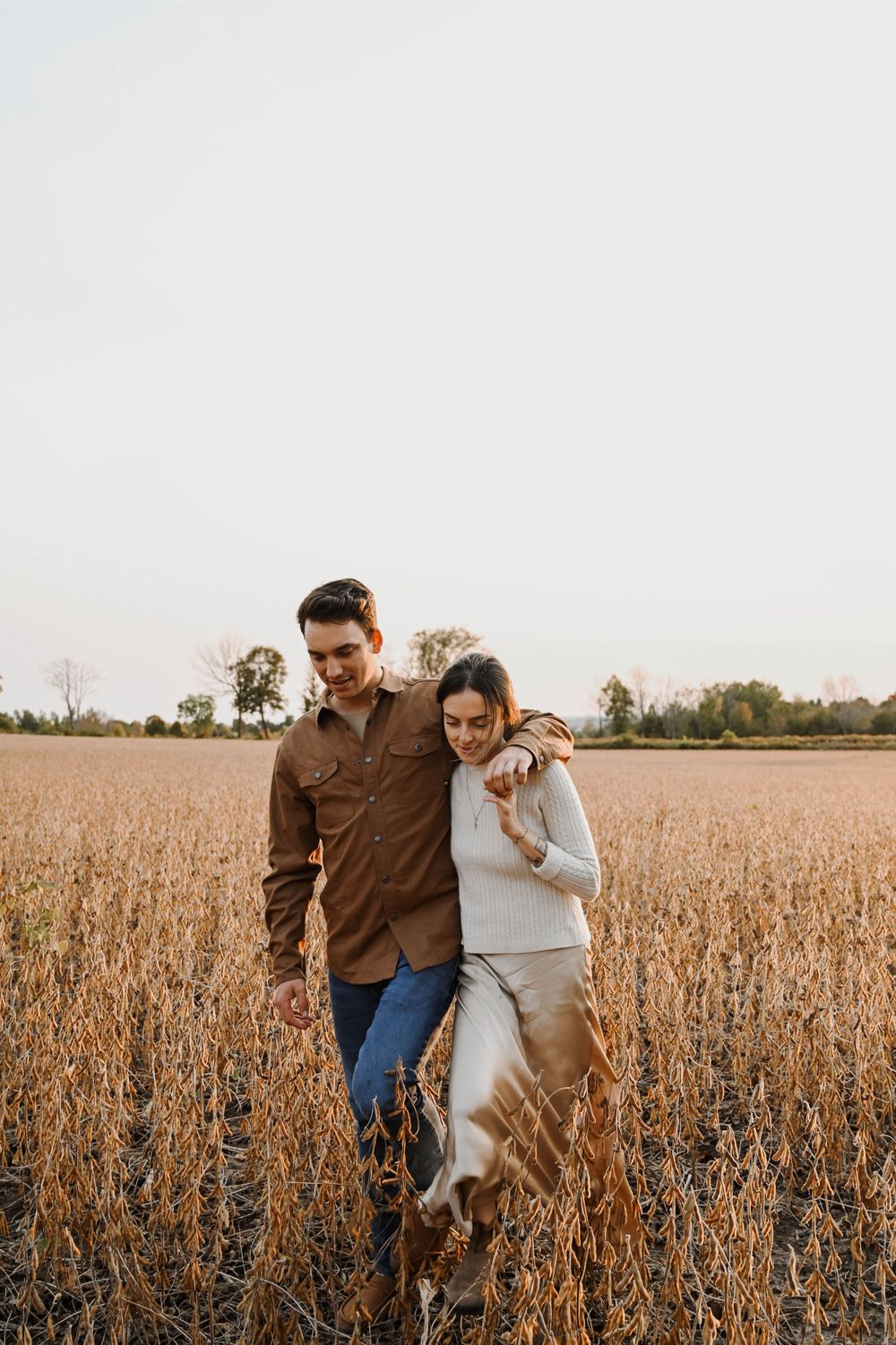 Couple walking together through a golden autumn soybean field at sunset in casual fall attire.