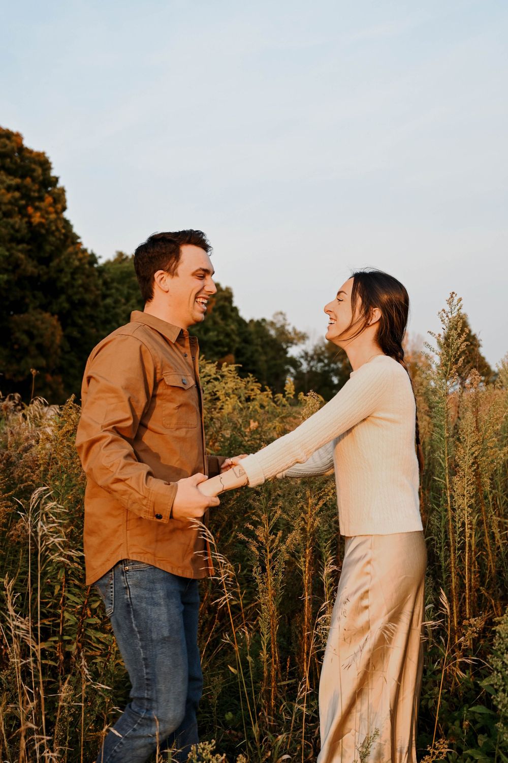 A couple shares a joyful moment together while holding hands in a golden field at sunset.