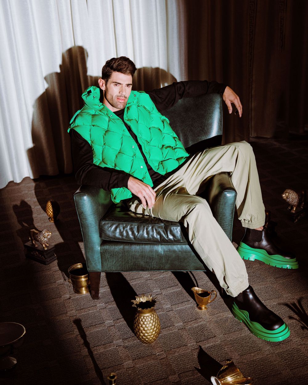 Lifestyle photo of model in bright green jacket lounging on leather chair with pineapple decorations.