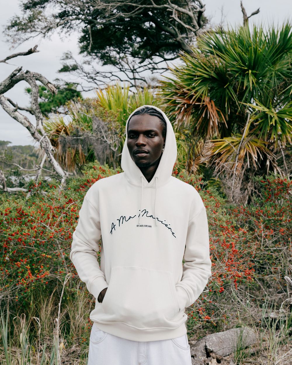 Person wearing white mountain graphic hoodie in coastal landscape with palm trees.