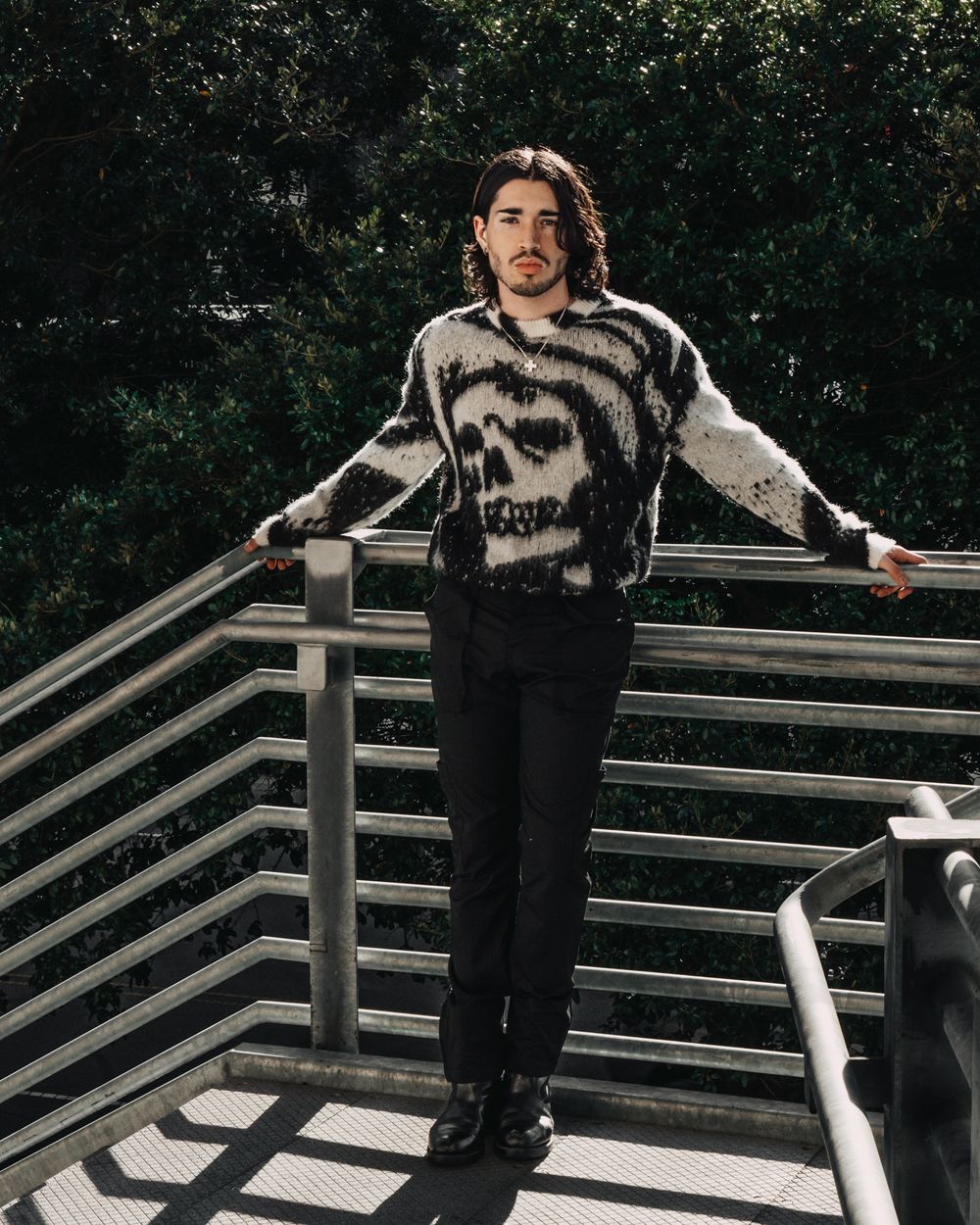 Person in a black and white patterned sweater posing on an outdoor staircase with metal railings.