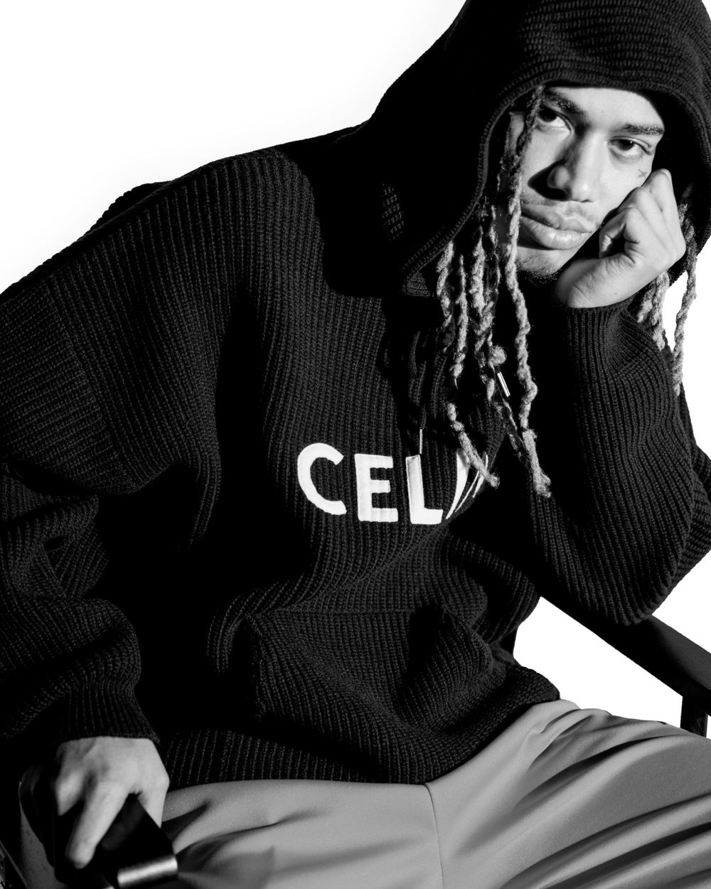 Portrait of someone in a black CELINE sweater and beanie with braided hair in black and white.