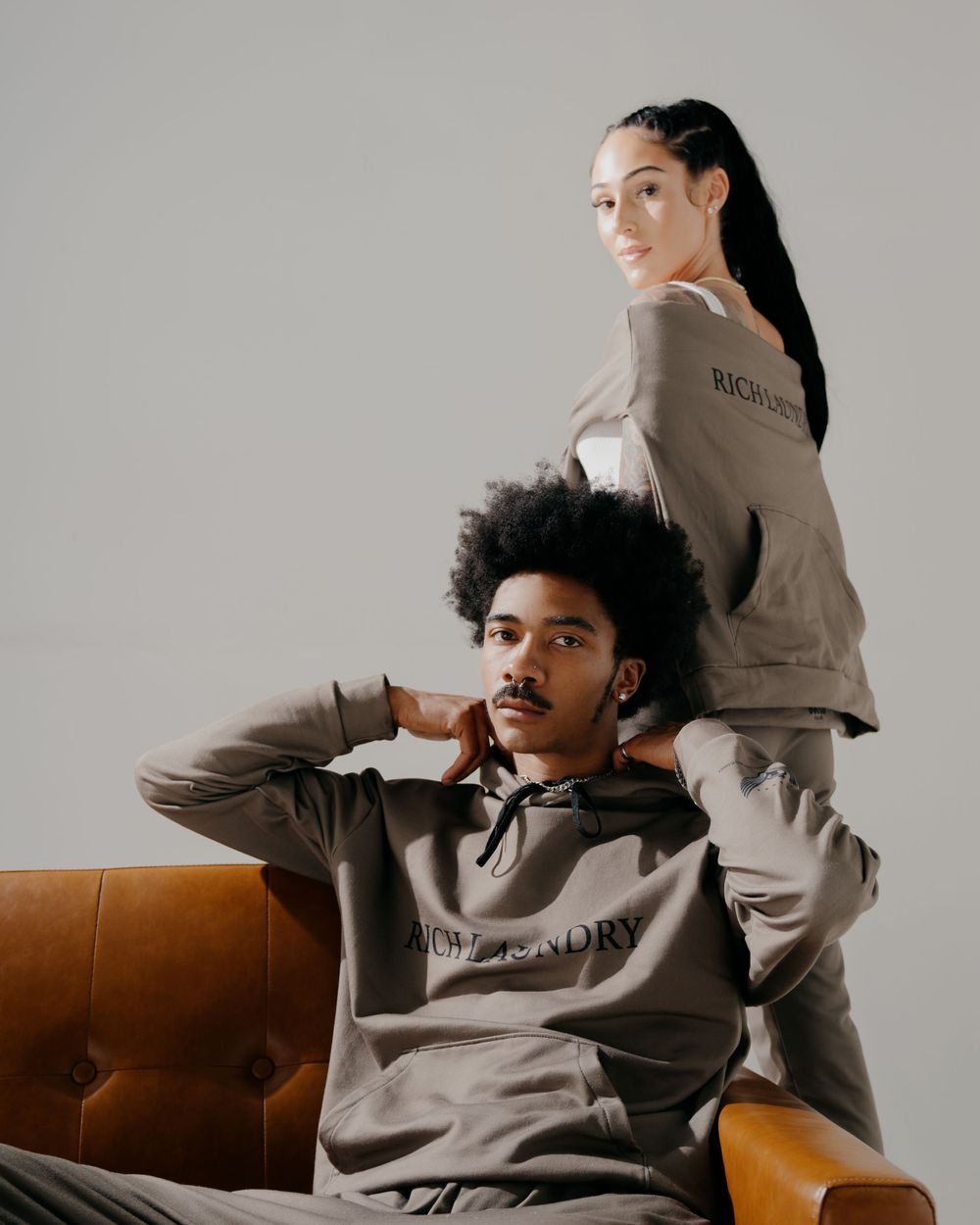 Two models wearing matching beige loungewear in minimalist studio setting.