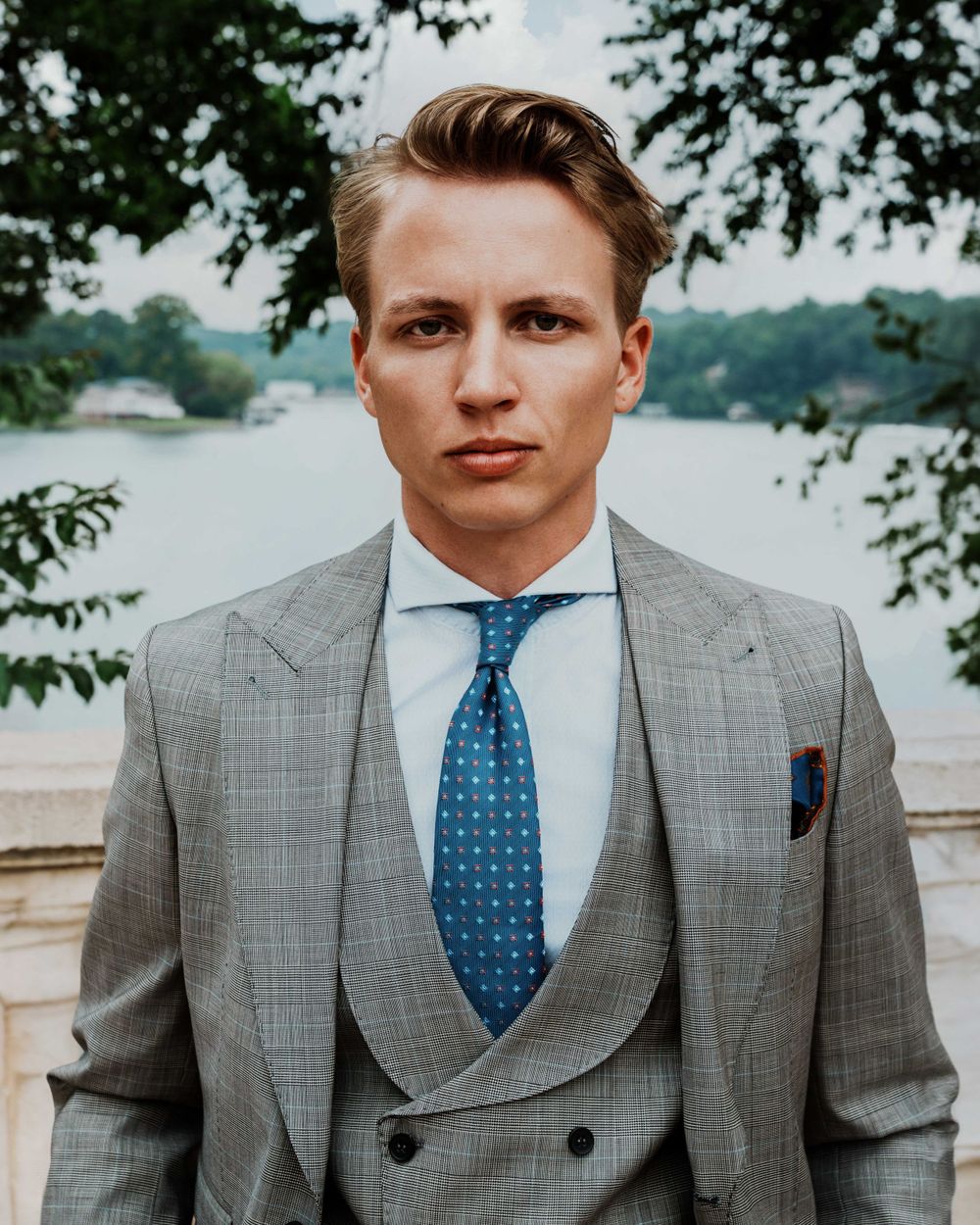 Portrait of someone in gray suit with blue polka dot tie against waterfront background.