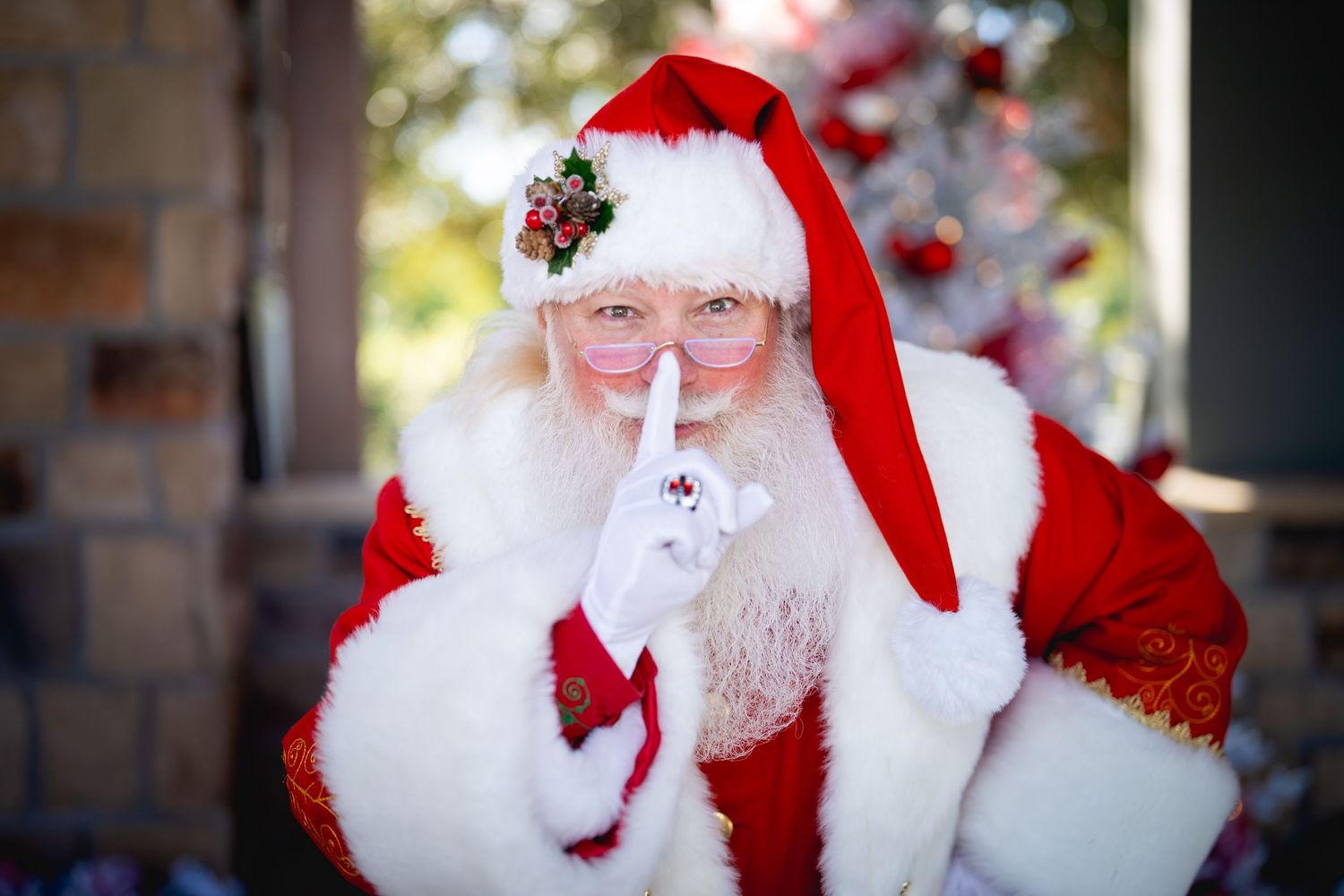 Someone in a traditional red and white Santa Claus costume makes a shushing gesture with finger to lips.