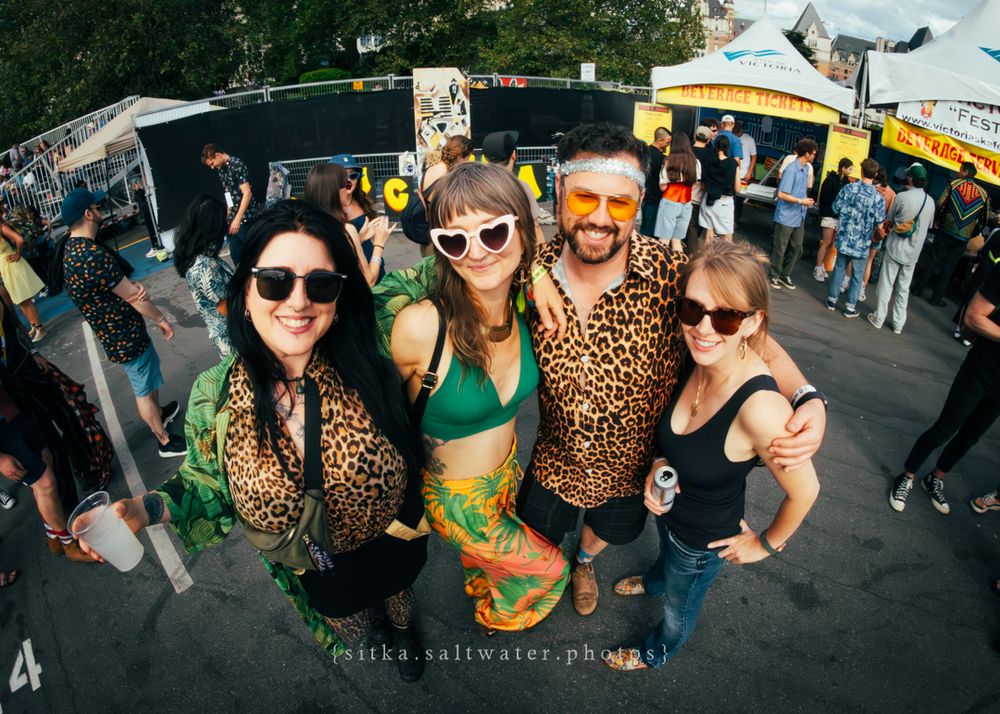 Festival goers in leopard print outfits and sunglasses pose together at an outdoor summer event with food trucks visible behind them.