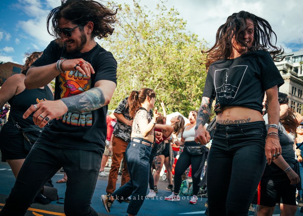 Energetic dancers in black t-shirts and jeans performing together at an outdoor event.