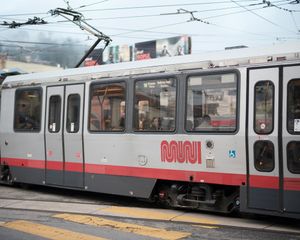 White and red MUNI light rail train car stopped at a transit station.