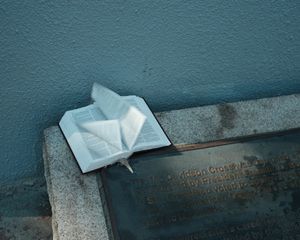 An open white book rests against a blue-green wall creating dramatic shadows.