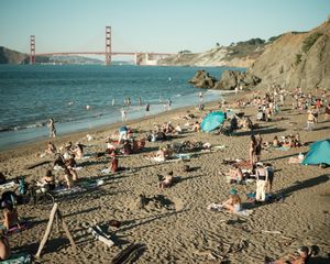 Beach-goers enjoy Baker Beach with the Golden Gate Bridge visible in the background on a sunny day.