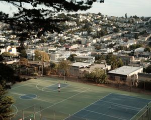 Blue basketball court overlooking dense urban hillside neighborhood.