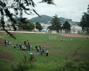 Groups of people gather on a grassy field for a recreational sports game surrounded by hills.