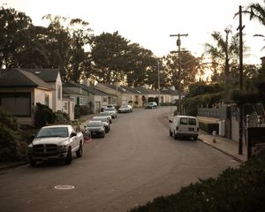 A residential street lined with parked cars and houses at sunset.